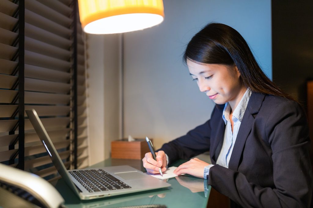 Businesswoman writing on paper with laptop computer